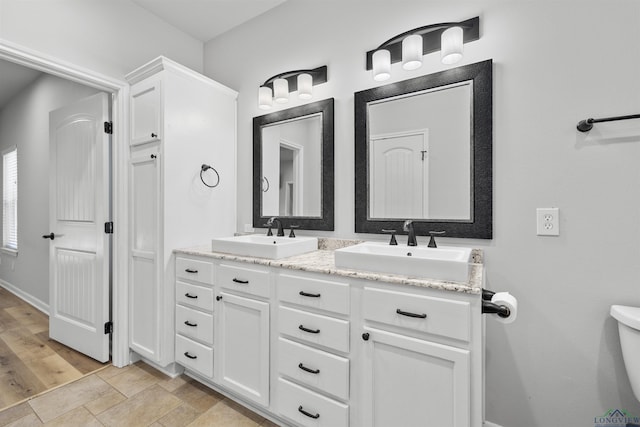 bathroom featuring double vanity, toilet, baseboards, and a sink