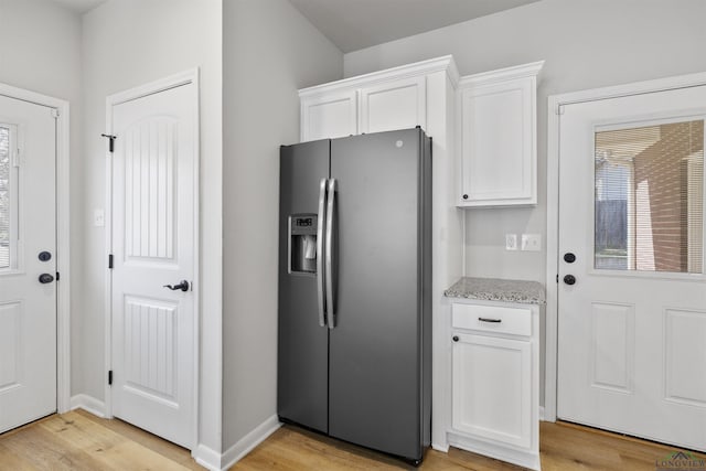 kitchen featuring light stone counters, baseboards, light wood finished floors, stainless steel fridge with ice dispenser, and white cabinets