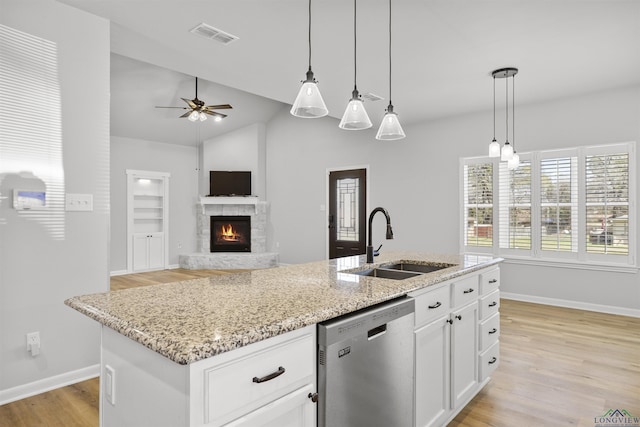 kitchen with a sink, white cabinets, light wood finished floors, light stone countertops, and dishwasher