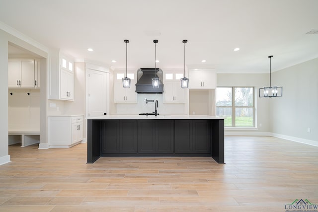 kitchen featuring white cabinetry, sink, premium range hood, an island with sink, and decorative light fixtures