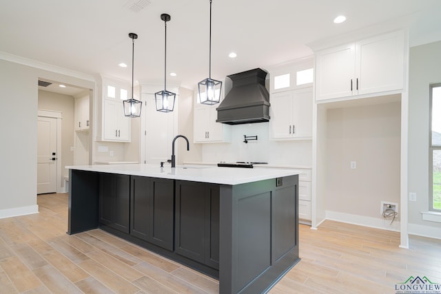 kitchen with decorative light fixtures, premium range hood, white cabinetry, and a center island with sink