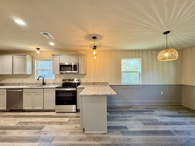 kitchen with visible vents, wainscoting, appliances with stainless steel finishes, a peninsula, and a sink