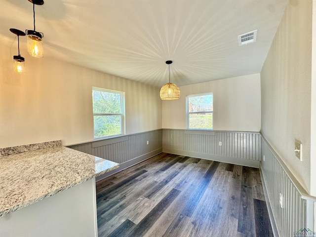 unfurnished dining area featuring dark wood-type flooring, visible vents, and a wainscoted wall