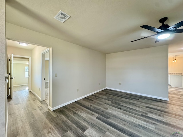 empty room with a ceiling fan, wood finished floors, visible vents, and baseboards