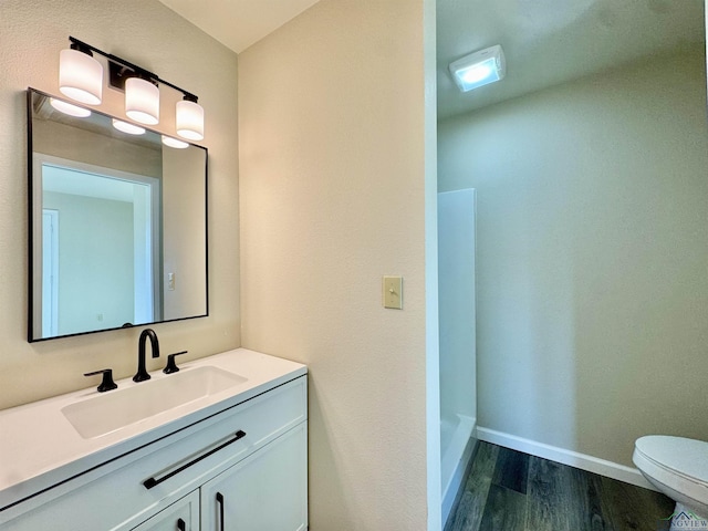 bathroom featuring toilet, wood finished floors, baseboards, walk in shower, and vanity