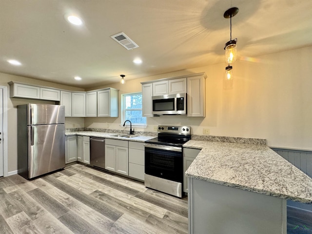 kitchen with visible vents, a peninsula, light wood-style flooring, a sink, and stainless steel appliances