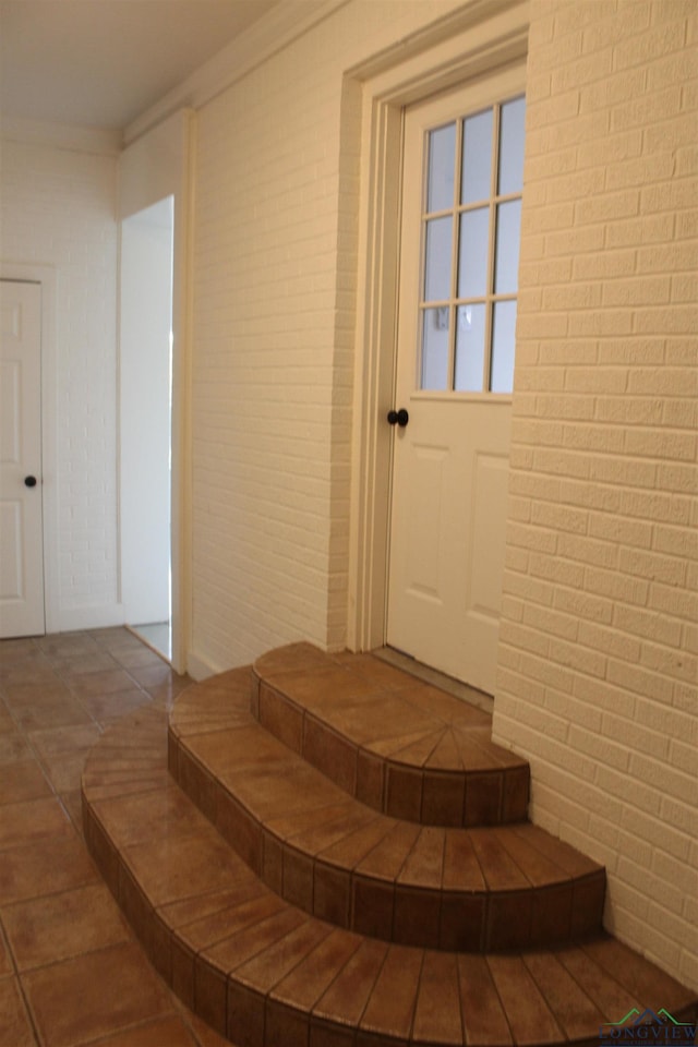 stairway featuring tile patterned floors, crown molding, and brick wall