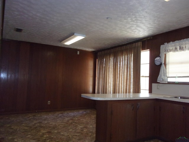 kitchen with kitchen peninsula, carpet, a textured ceiling, and wood walls