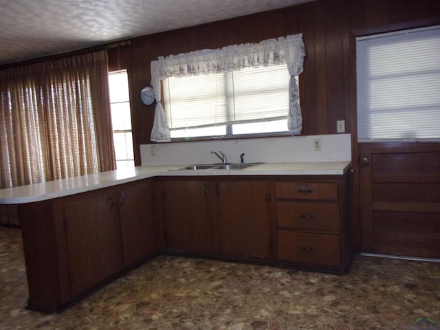 kitchen with sink, kitchen peninsula, a textured ceiling, wooden walls, and dark brown cabinets