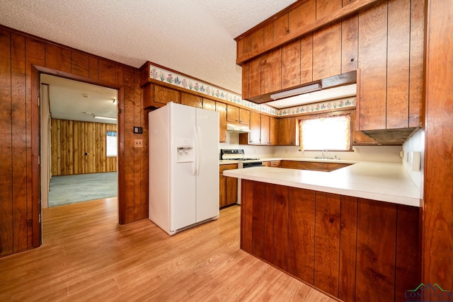 kitchen with kitchen peninsula, a textured ceiling, white refrigerator with ice dispenser, light hardwood / wood-style flooring, and wood walls