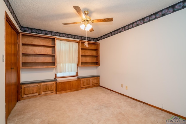 unfurnished office featuring light carpet, a textured ceiling, and ceiling fan