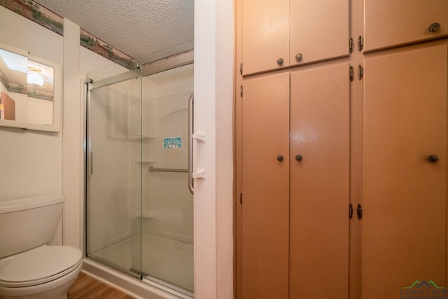 bathroom with wood-type flooring, a textured ceiling, toilet, and a shower with door