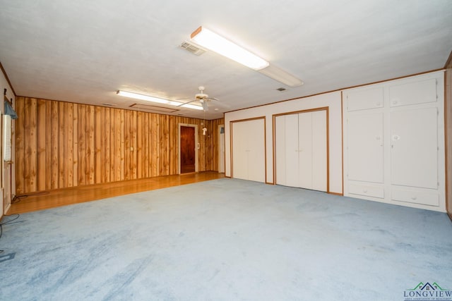 basement featuring carpet flooring, ceiling fan, and wooden walls