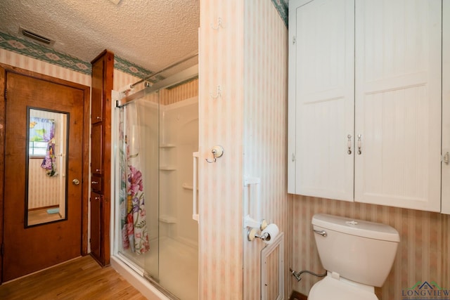 bathroom featuring a textured ceiling, hardwood / wood-style flooring, toilet, and an enclosed shower