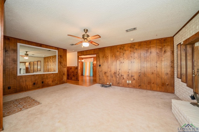 unfurnished living room with wooden walls, brick wall, light colored carpet, and a textured ceiling