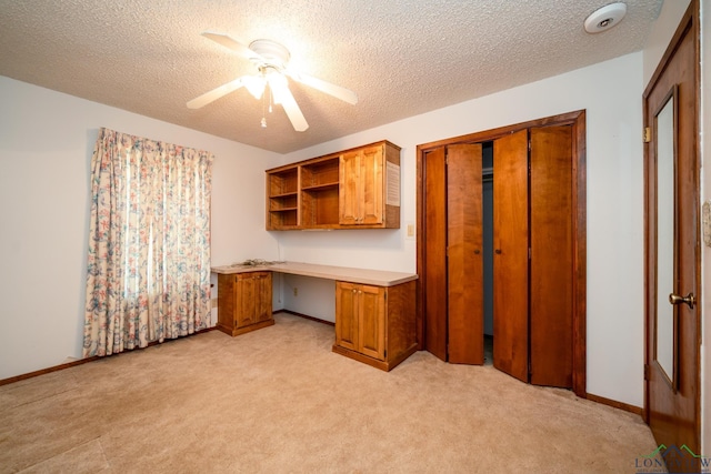 unfurnished office with ceiling fan, light colored carpet, built in desk, and a textured ceiling