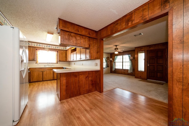 kitchen with kitchen peninsula, a textured ceiling, a healthy amount of sunlight, wooden walls, and white fridge with ice dispenser