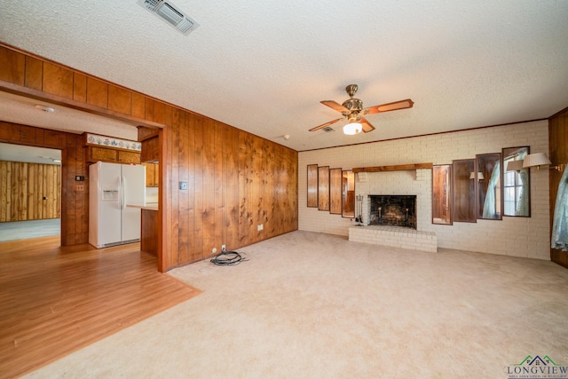 unfurnished living room featuring wooden walls, a brick fireplace, ceiling fan, a textured ceiling, and brick wall