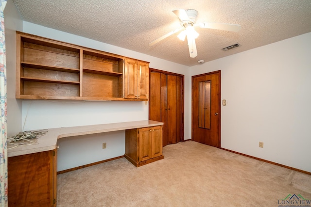 unfurnished office with ceiling fan, light colored carpet, built in desk, and a textured ceiling