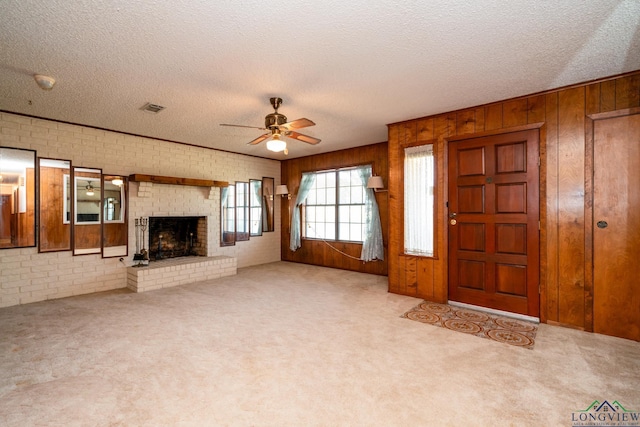 unfurnished living room featuring wooden walls, ceiling fan, light colored carpet, and brick wall