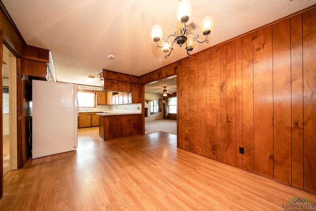 kitchen featuring white refrigerator, decorative light fixtures, a wealth of natural light, and wood walls