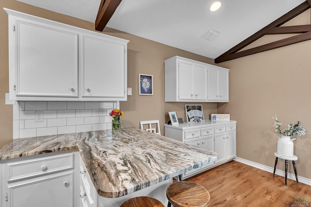 kitchen featuring visible vents, light stone countertops, light wood-type flooring, white cabinetry, and lofted ceiling with beams