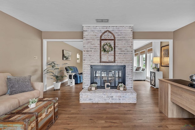 living room with baseboards, wood finished floors, visible vents, and a fireplace