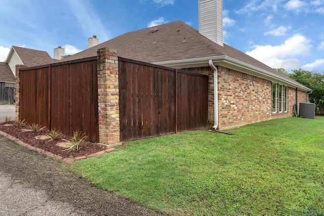 view of side of home featuring central AC, a chimney, brick siding, a shingled roof, and a lawn