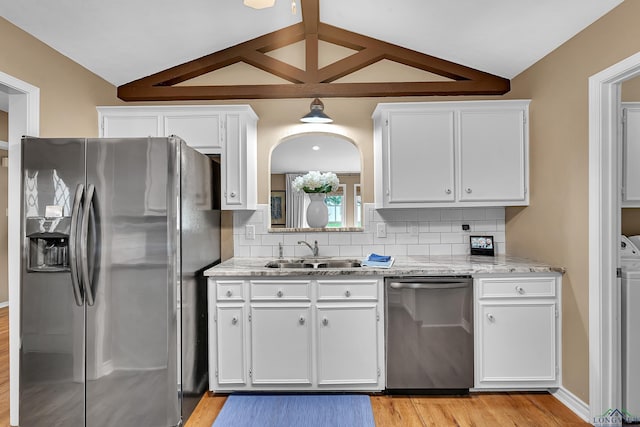 kitchen with appliances with stainless steel finishes, a sink, lofted ceiling, light wood-style floors, and white cabinetry