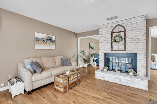 living area with baseboards, a brick fireplace, wood finished floors, and visible vents
