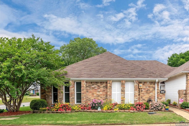 exterior space with brick siding, a front yard, and roof with shingles