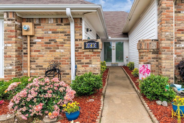 entrance to property featuring a shingled roof and brick siding