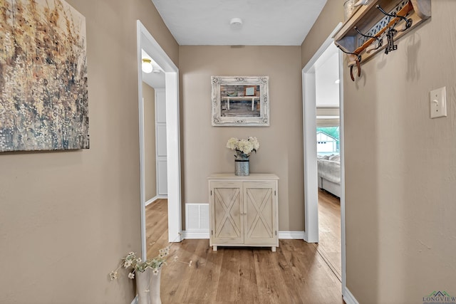 hall featuring baseboards, wood finished floors, and visible vents