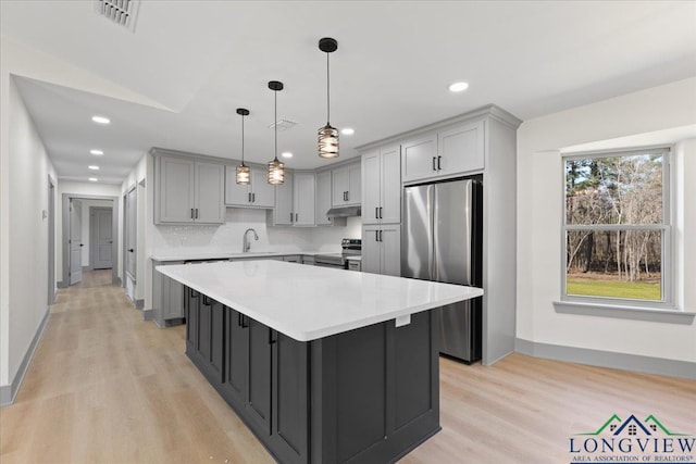 kitchen with gray cabinetry, stainless steel appliances, a sink, and under cabinet range hood