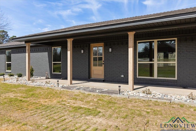 view of exterior entry with covered porch, brick siding, and a lawn