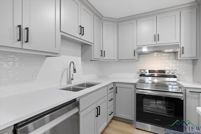 kitchen with gray cabinetry, under cabinet range hood, a sink, light countertops, and appliances with stainless steel finishes