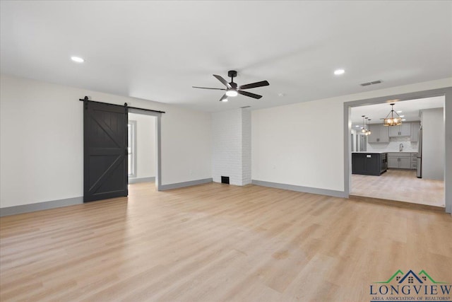 unfurnished living room with a barn door, visible vents, baseboards, light wood-style flooring, and ceiling fan with notable chandelier