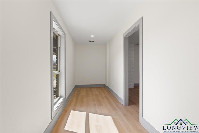 hall featuring baseboards, visible vents, and light wood finished floors