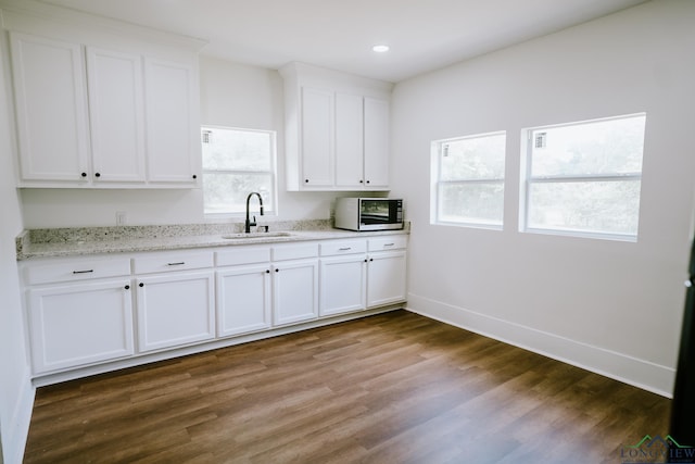kitchen featuring white cabinets, dark wood finished floors, light stone counters, a sink, and baseboards