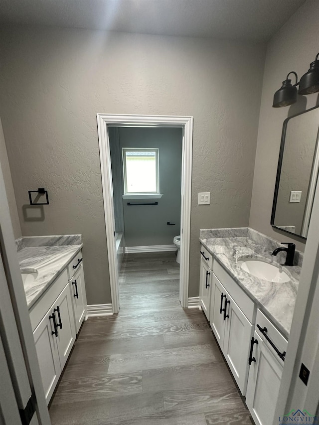 153 Heartland Xing, Diana, TX 75640 - bathroom with two vanities, toilet, wood finished floors, baseboards, and a textured wall