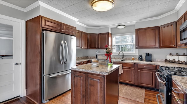 kitchen featuring stainless steel appliances, wood finished floors, a kitchen island, a sink, and ornamental molding