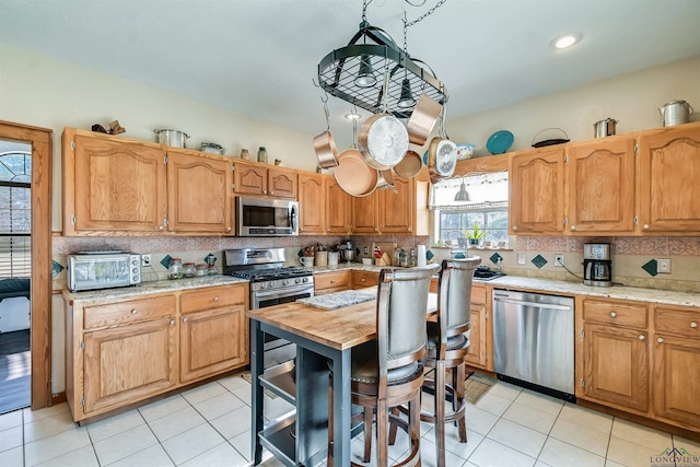 kitchen with light tile patterned floors, stainless steel appliances, a toaster, and decorative backsplash