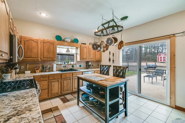 kitchen with light tile patterned floors, stainless steel appliances, a sink, brown cabinets, and tasteful backsplash