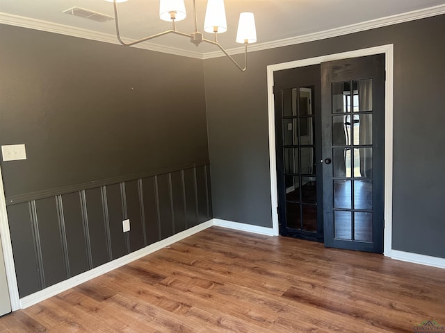 spare room featuring wood-type flooring, ornamental molding, and an inviting chandelier