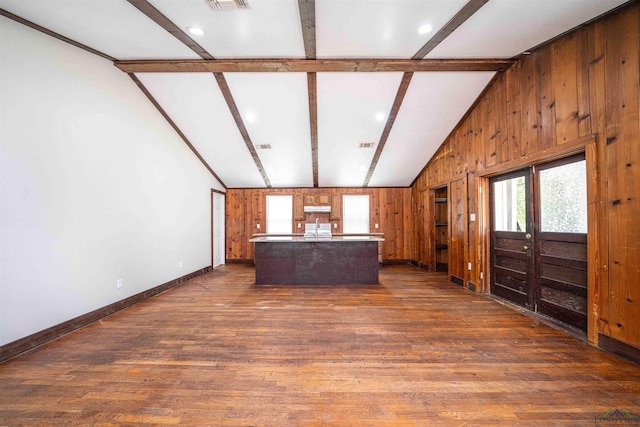 unfurnished living room with dark wood finished floors, wood walls, a healthy amount of sunlight, and vaulted ceiling with beams