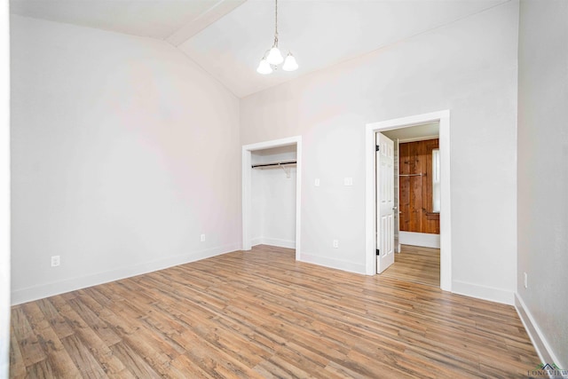 unfurnished bedroom with vaulted ceiling, wood finished floors, an inviting chandelier, baseboards, and ensuite bath
