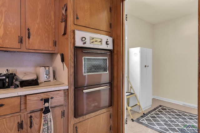 kitchen featuring baseboards, a warming drawer, light countertops, and brown cabinetry