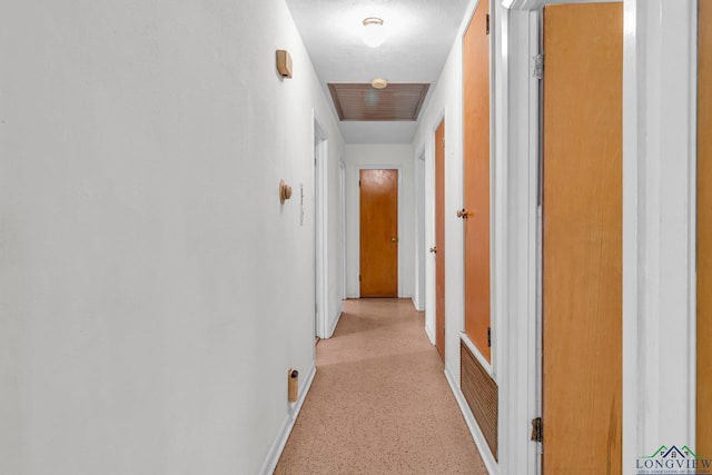 hall featuring visible vents, baseboards, and light speckled floor