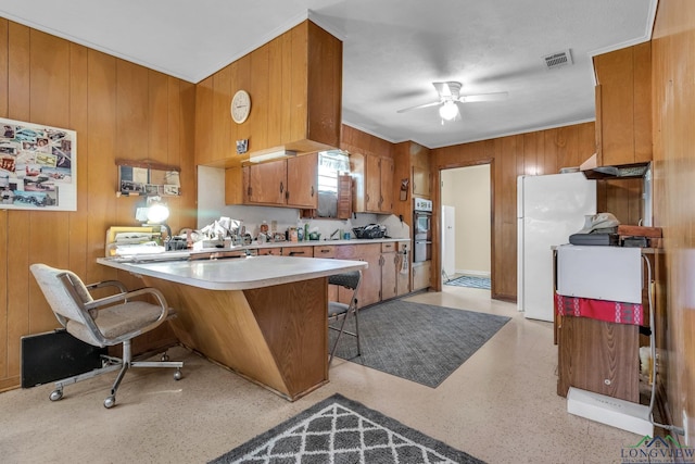 kitchen featuring visible vents, light countertops, freestanding refrigerator, brown cabinetry, and wood walls