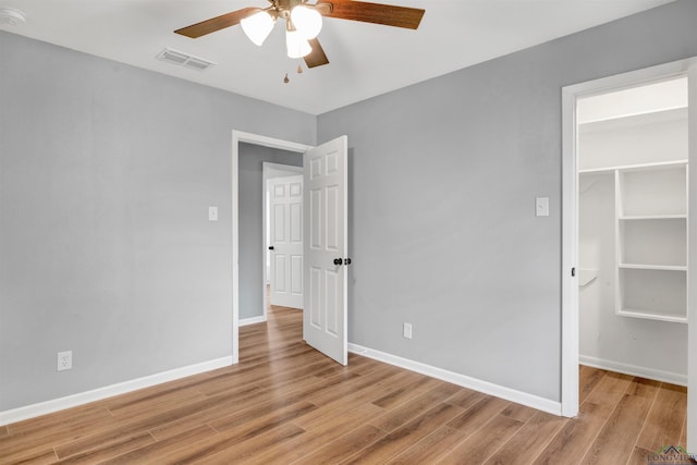 unfurnished bedroom featuring light wood-type flooring, a walk in closet, visible vents, and baseboards